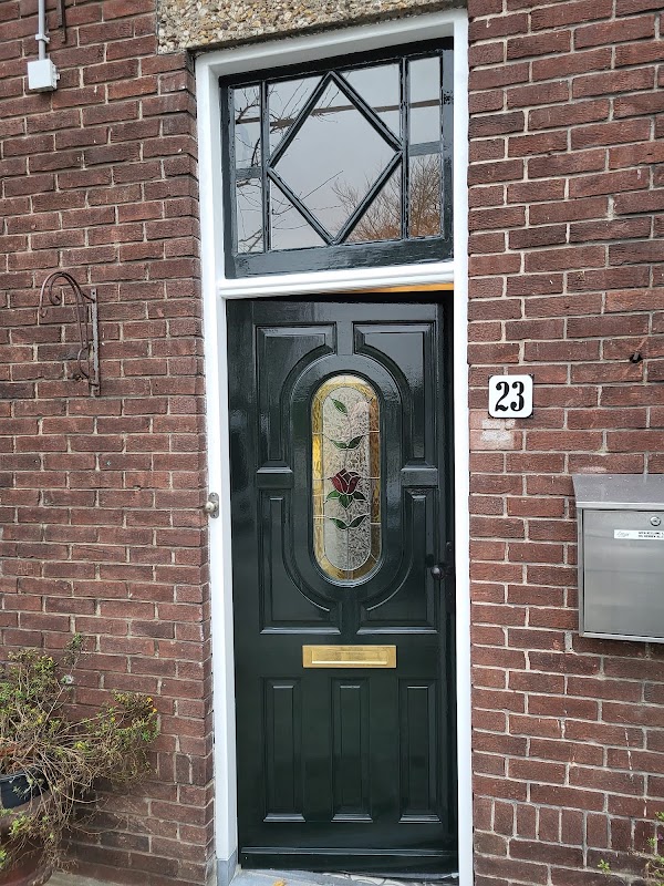 Donkergroen geschilderde voordeur met glas-in-lood bovenlicht en messing brievenbus.